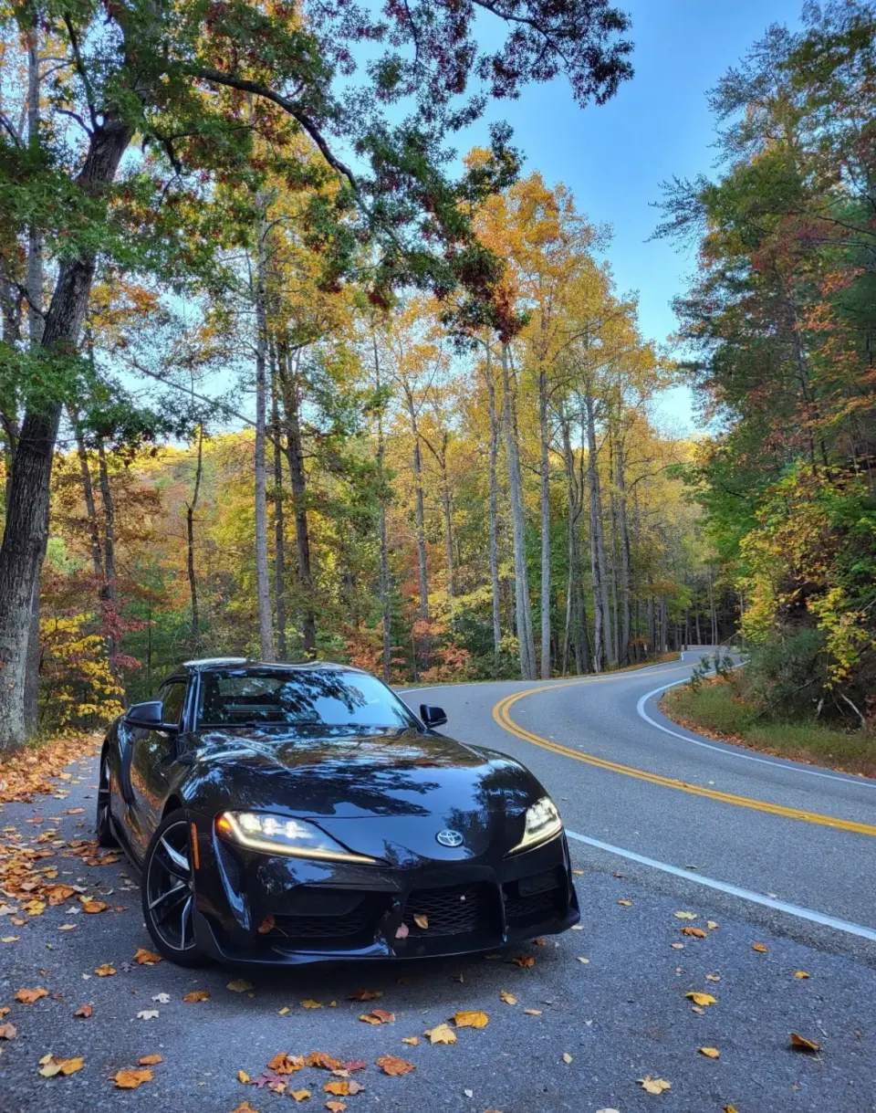 Black Toyota GR Supra on a winding road in fall colors