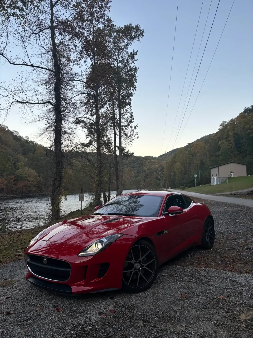 Red Jaguar F-Type coupe parked by a river at dusk