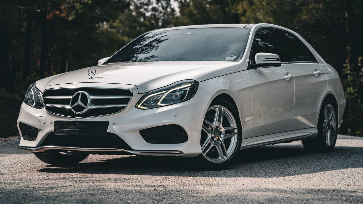 White Mercedes-Benz E-Class parked outdoors beside trees
